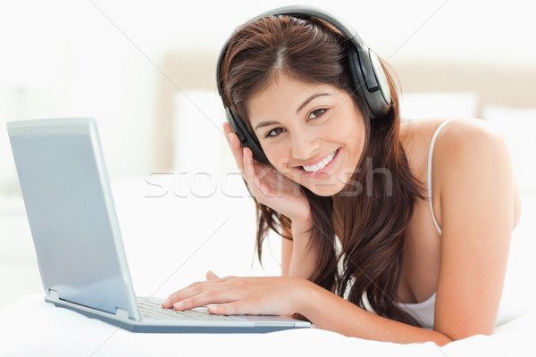 A woman looking forward and smiling as she uses a laptop and listens to headphones as she relaxs on  Stock photo © wavebreak_media