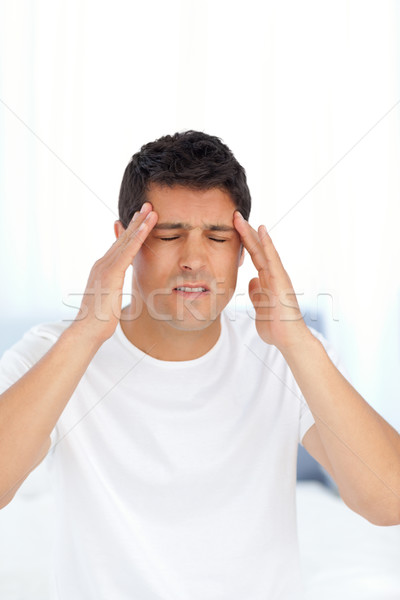 Stock photo: Man massaging his temples sitting on his bed at home