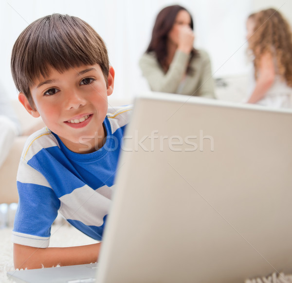 Stock photo: Young boy using laptop on the carpet with his family behind him