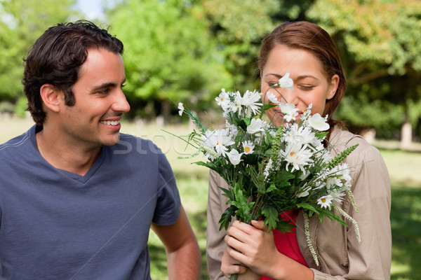 Man happily smiling as he watches his friend smell a bunch of flowers in a bright grassland area Stock photo © wavebreak_media