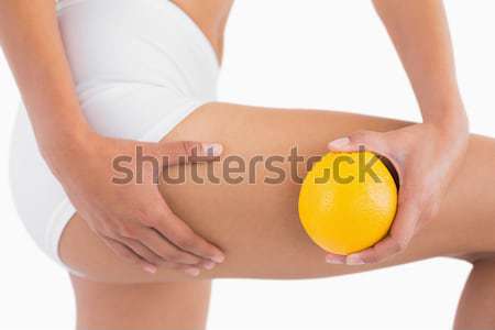 Woman squeezes cellulite skin on thigh as she holds orange Stock photo © wavebreak_media