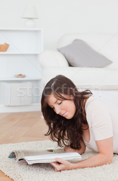 Stock photo: Young pretty woman reading a magazine while lying on a carpet in the living room