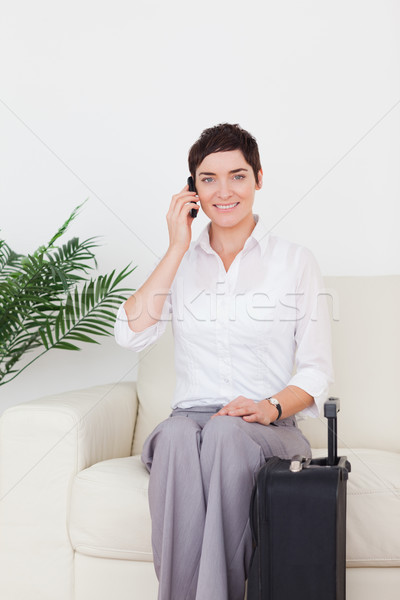 Stock photo: Short-haired woman on the phone with a suitcase in a waiting room