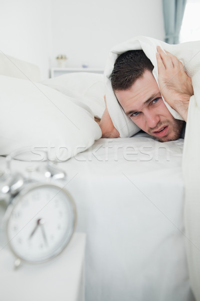 Portrait of a man covering his ears with a duvet while his alarm clock is ringing in his bedroom Stock photo © wavebreak_media