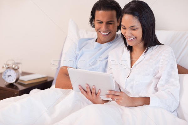 Stock photo: Young couple sitting on the bed using tablet pc