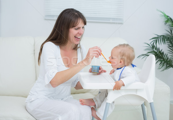 Stock photo: Mother sitting in a sofa while feeding a baby in living room