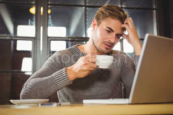 Stock photo: Overworked man drinking coffee and looking at laptop