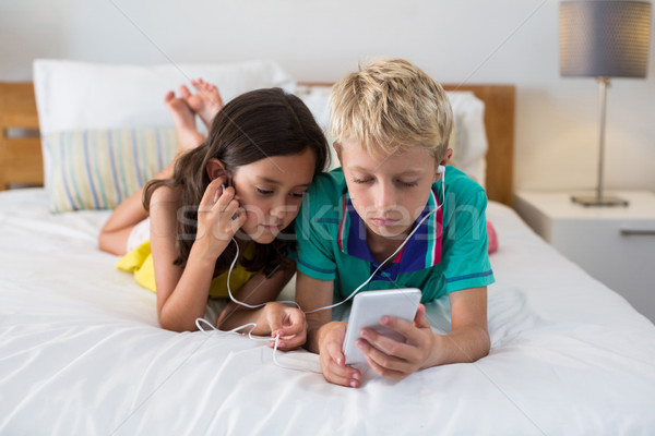 Siblings listening to music while using mobile phone on bed Stock photo © wavebreak_media