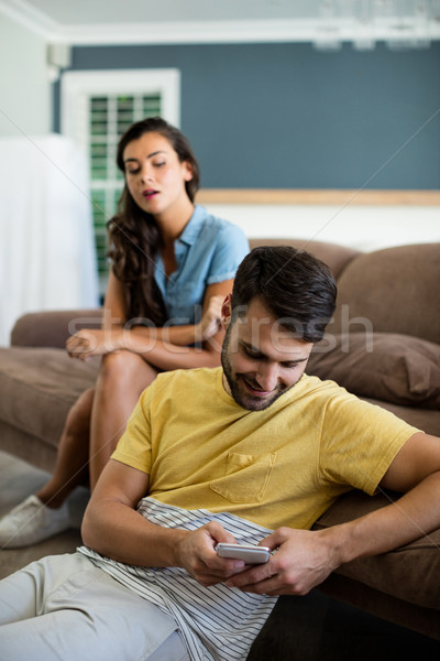 Jealous woman watching man using mobile phone in the living room Stock photo © wavebreak_media