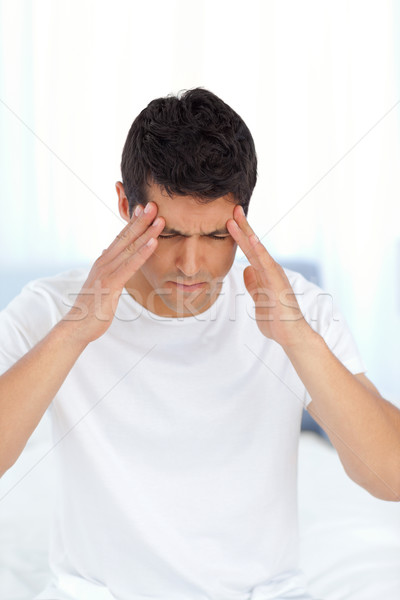 Stock photo: Handsome man having a headache sitting on his bed at home