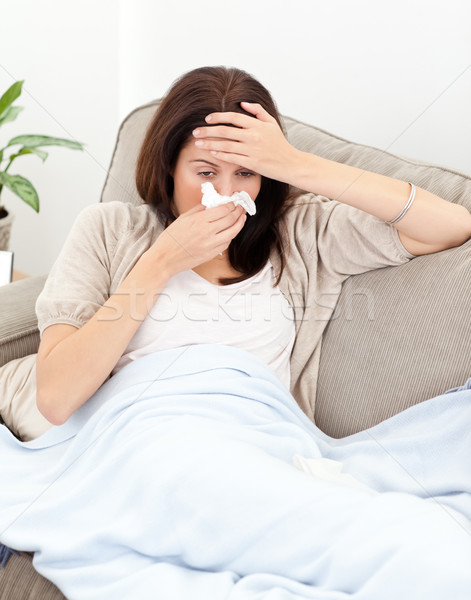 Tired woman feeling her temperature while blowing her nose on the sofa Stock photo © wavebreak_media