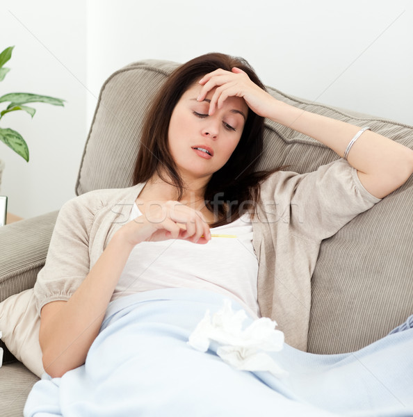 Sick woman looking at a thermometer while resting on the sofa at home Stock photo © wavebreak_media