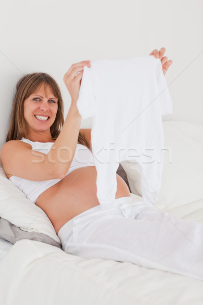 Beautiful pregnant female showing a little white pyjama while lying on a bed in her apartment Stock photo © wavebreak_media