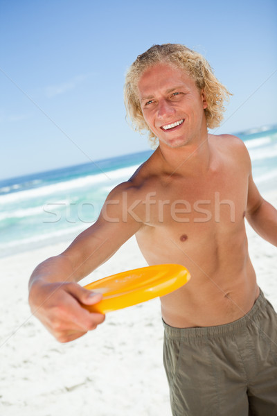 Stock photo: Smiling blonde man standing up while playing with a yellow frisbee
