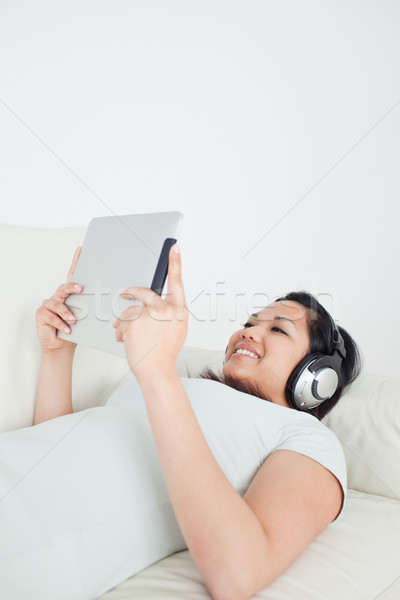 Woman lying on a sofa with headphones on and holding a tactile tablet in a living room Stock photo © wavebreak_media