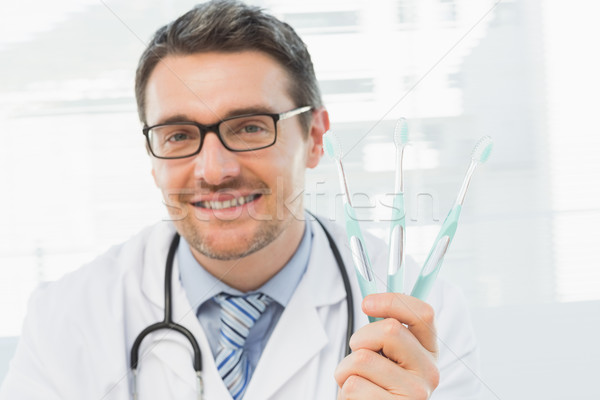 Smiling doctor holding toothbrushes in office Stock photo © wavebreak_media