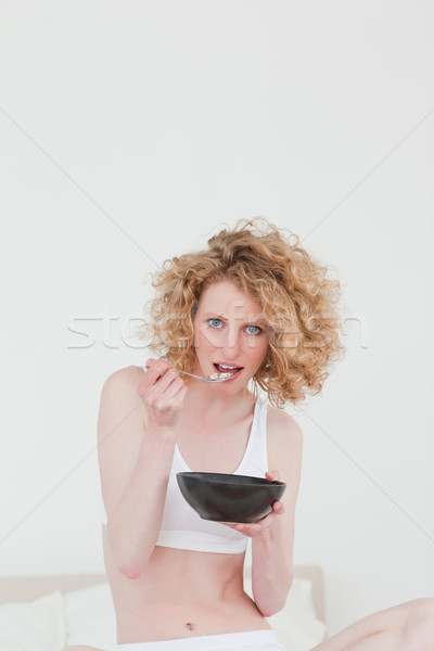Gorgeous blonde woman eating a bowl of cereals while sitting on her bed in her appartment Stock photo © wavebreak_media