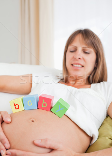 Beautiful pregnant female playing with wooden blocks while lying on a sofa in her living room Stock photo © wavebreak_media