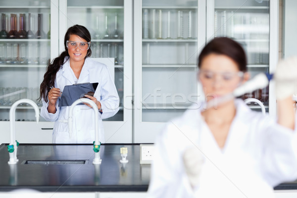 Female scientist writing on a clipboard while her colleague is pouring a liquid in a tube Stock photo © wavebreak_media