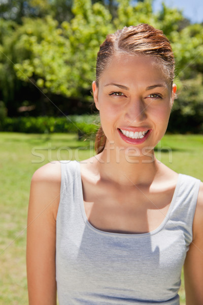 Woman dressed in workout gear smiling while looking straight ahead with trees and grass in the backg Stock photo © wavebreak_media