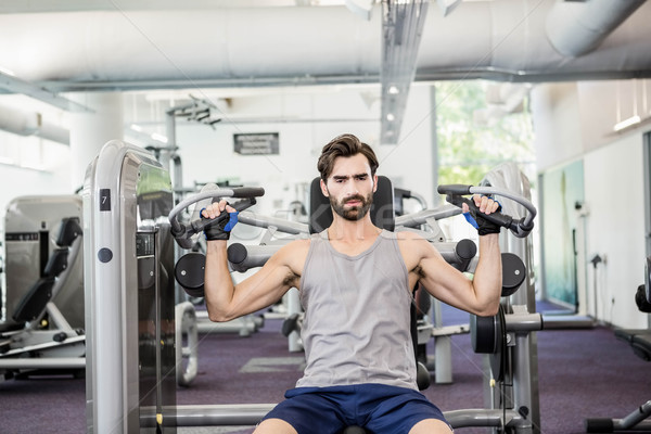 Stock photo: Focused man using weights machine for arms