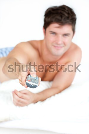 Good-looking man holding a remote lying on his bed Stock photo © wavebreak_media