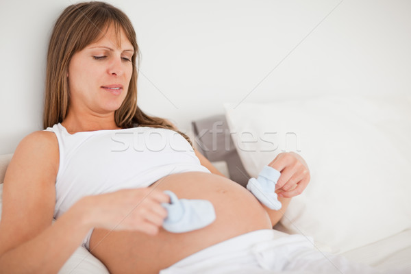Stock photo: Good looking pregnant woman playing with little socks while lying on a bed in her apartment