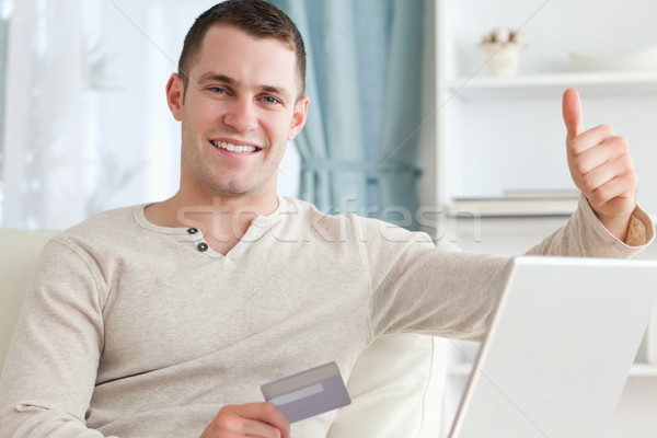 Smiling man shopping online with the thumb up in his living room Stock photo © wavebreak_media