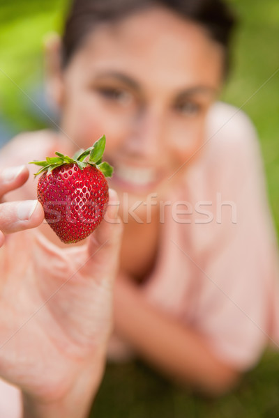 Woman holds a strawberry at arms reach while lying prone in grass with focus on the stawberry Stock photo © wavebreak_media