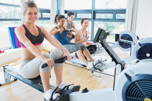 Smiling woman on rowing machine with others in fitness studio Stock photo © wavebreak_media