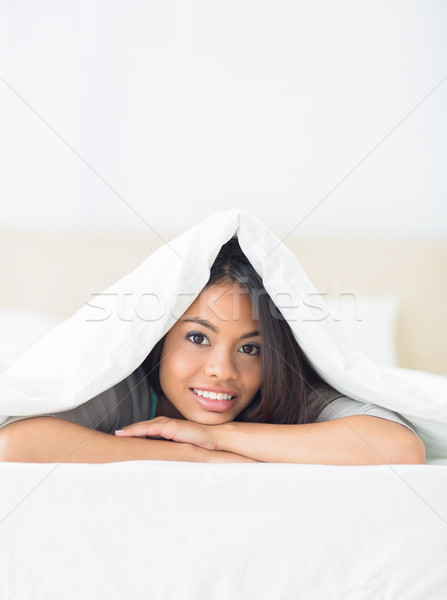 Happy girl lying under the duvet smiling at camera Stock photo © wavebreak_media