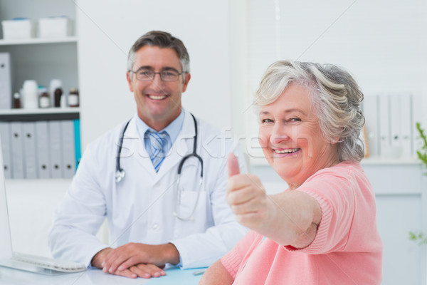 Patient showing thumbs up sign while sitting with doctor Stock photo © wavebreak_media
