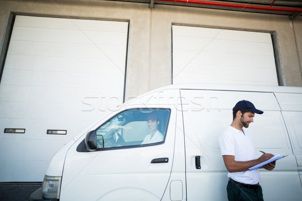 Delivery man writing on clipboard while standing next to his van Stock photo © wavebreak_media