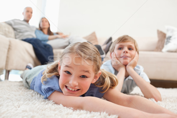 Stock photo: Siblings lying on a carpet while their parents are sitting on a sofa