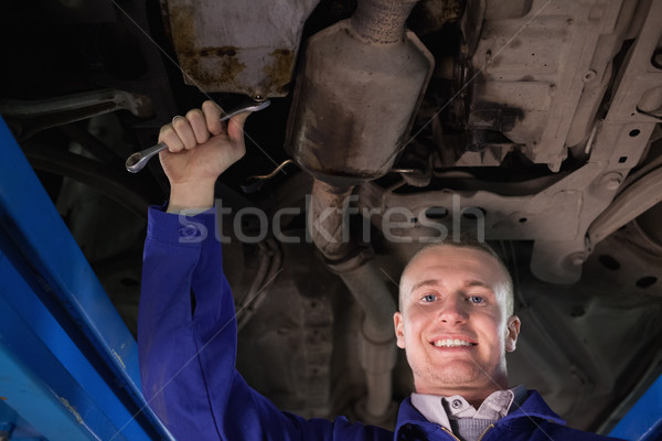 Stock photo: Mechanic looking at camera below a car in a garage