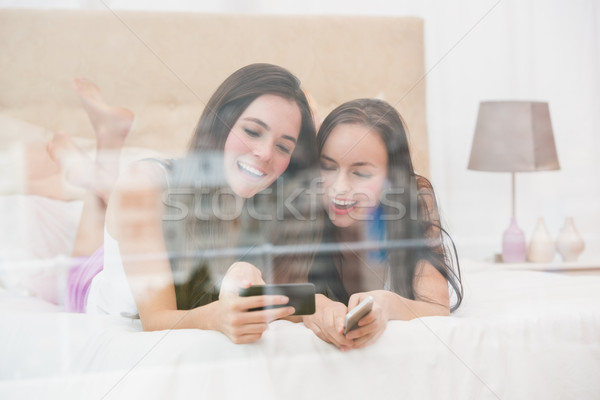 Pretty friends looking at smartphone on bed Stock photo © wavebreak_media