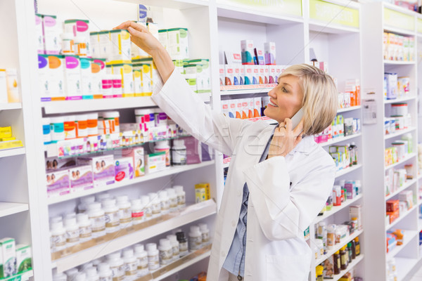 Smiling pharmacist phoning and taking medicine from shelf Stock photo © wavebreak_media