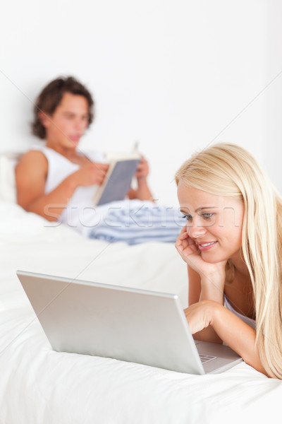 Portrait of a woman using a notebook while her fiance is reading on their bed Stock photo © wavebreak_media