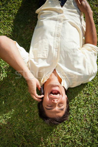 Stock photo: Man with his eyes closed laughing while using a mobile phone as he lies down on the grass