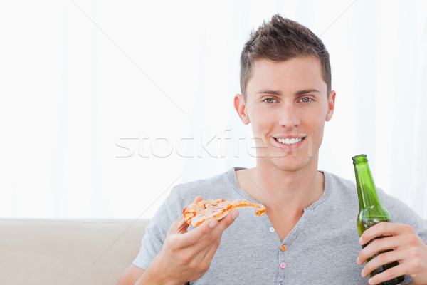 A smiling man looking at the camera as he eats pizza and holds some beer Stock photo © wavebreak_media