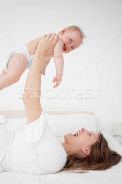 Happy woman holding her baby while lying in a bedroom Stock photo © wavebreak_media