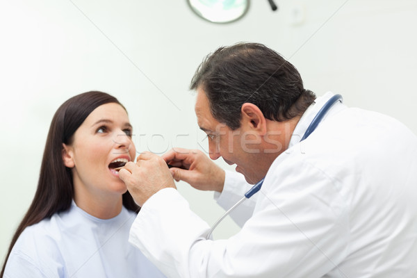 Stock photo: Doctor looking at the mouth of his patient in an examination room