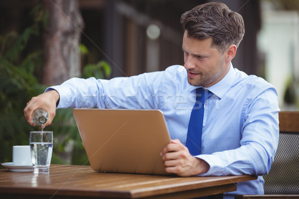 Handsome businessman pouring drink in glass while using laptop Stock photo © wavebreak_media