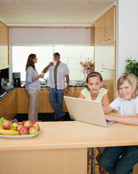 Stock photo: Siblings with their laptop in the kitchen with parents behind them