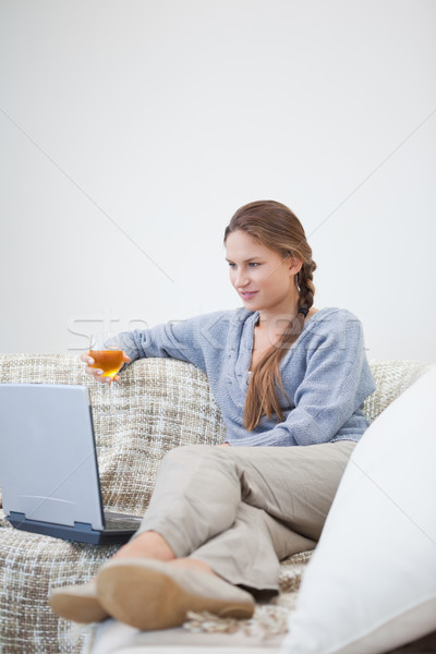 Woman sitting and holding a glass while looking on a laptop indoors Stock photo © wavebreak_media