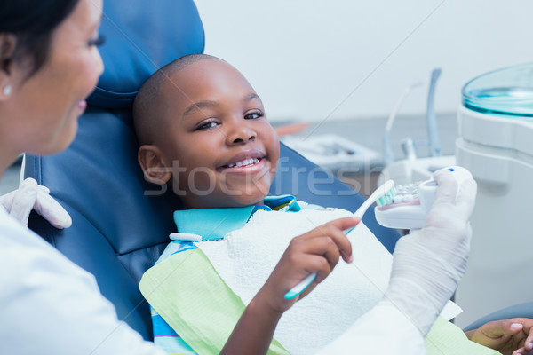 Dentist teaching happy boy how to brush teeth Stock photo © wavebreak_media