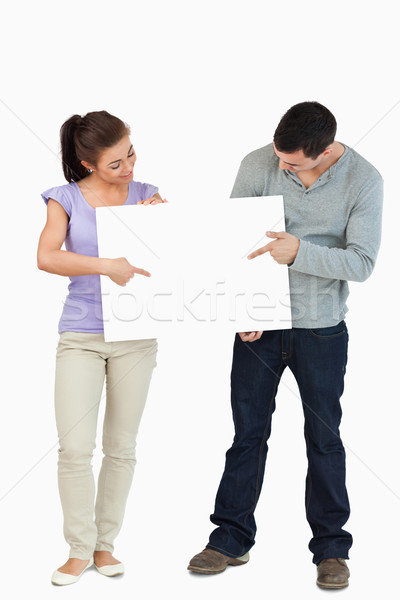 Young couple pointing at sign they are holding together against a white background Stock photo © wavebreak_media
