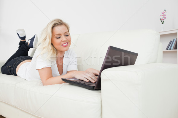 Stock photo: Woman working on a laptop while lying on the white sofa
