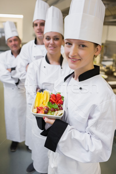 Smiling chef holding fruit plate with team of Chef's in kitchen Stock photo © wavebreak_media