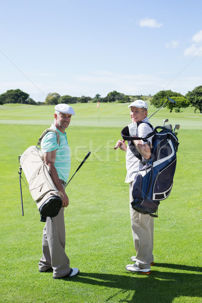 Golfer friends smiling at camera holding their golf bags Stock photo © wavebreak_media